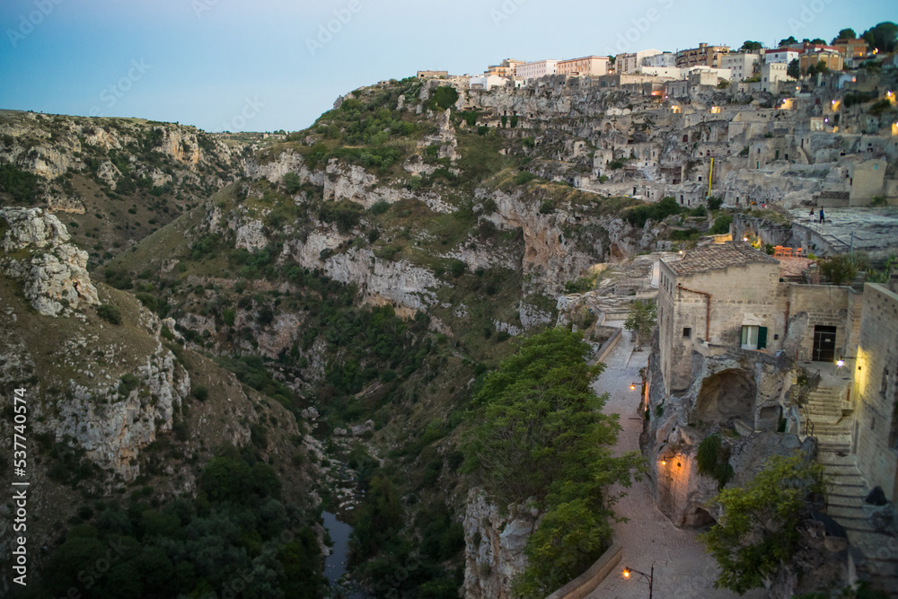 view after dark of old stone houses and churches on the slopes of the gorge in the historic center of the old town of Matera illuminated by street lamps. Cascade buildings of the old town with rocks 