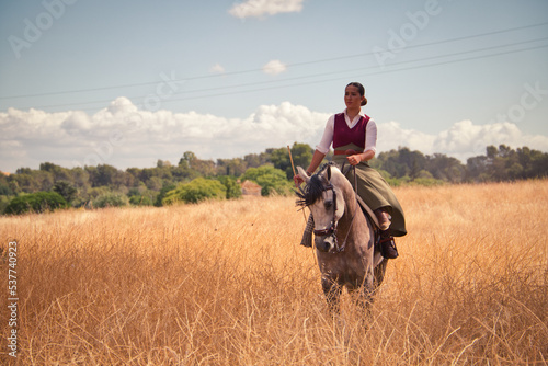 Young and beautiful Spanish woman on a Thoroughbred horse riding in the countryside in Spain. The woman is wearing a horse riding uniform. Thoroughbred and equine concept. © @skuder_photographer