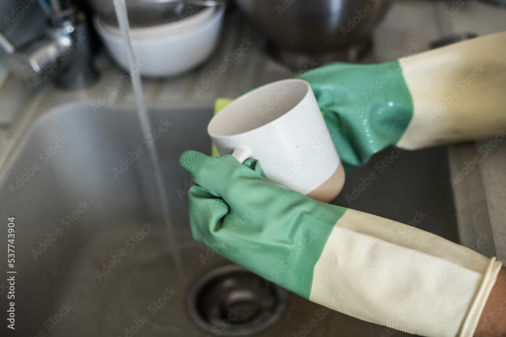 Cropped image of child washing dishes in rubber gloves