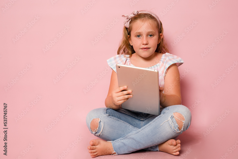 Young girl sitting on floor and using a tablet isolated over pink background. Young girl sitting on floor and using a tablet isolated over pink background.