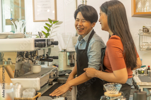 Female business owner works with her LGBT partner to prepare coffee or drink for customer in a coffee shop. A couple of LGBT startup help each other at a coffee counter for their business.
