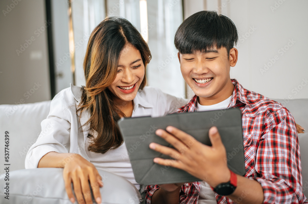 Young Asian couple enjoy with tablet together in living room Young Asian couple enjoy with tablet together in living room
