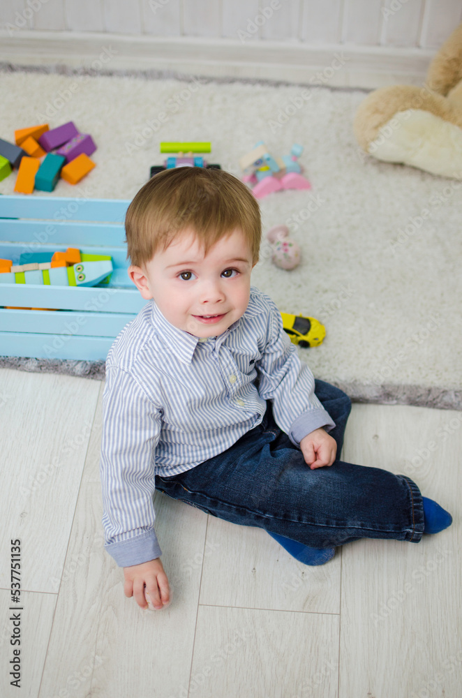 Fototapeta premium Boy 2 years old sits on a carpet in a children's room with toys