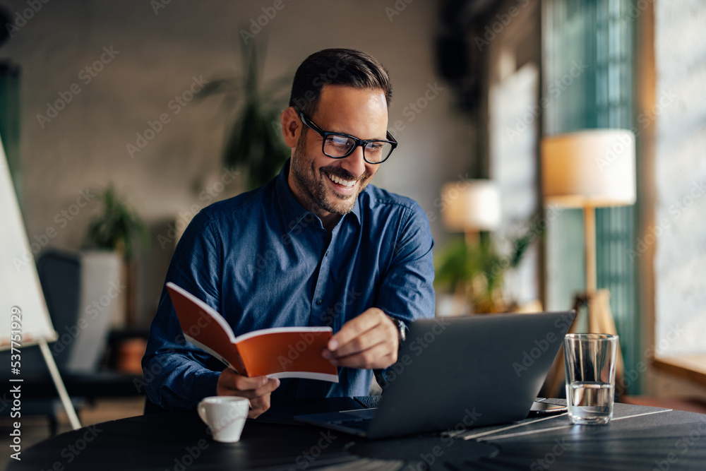 Male boss being at his office, looking at the laptop, holding a notebook. Male boss being at his office, looking at the laptop, holding a notebook.