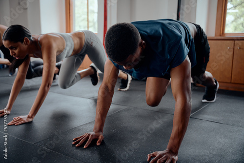 Young biracial woman and black man in sportswear doing mountain climbers at the gym