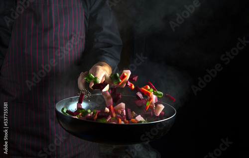 Cooking vegetables in a pan in a chef hand on a black background with copy space. Nutrition concept. Vegetable menu for the hotel
