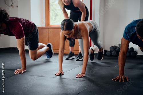 Group of determined multiracial young adults with trainer doing mountain climbers at the gym