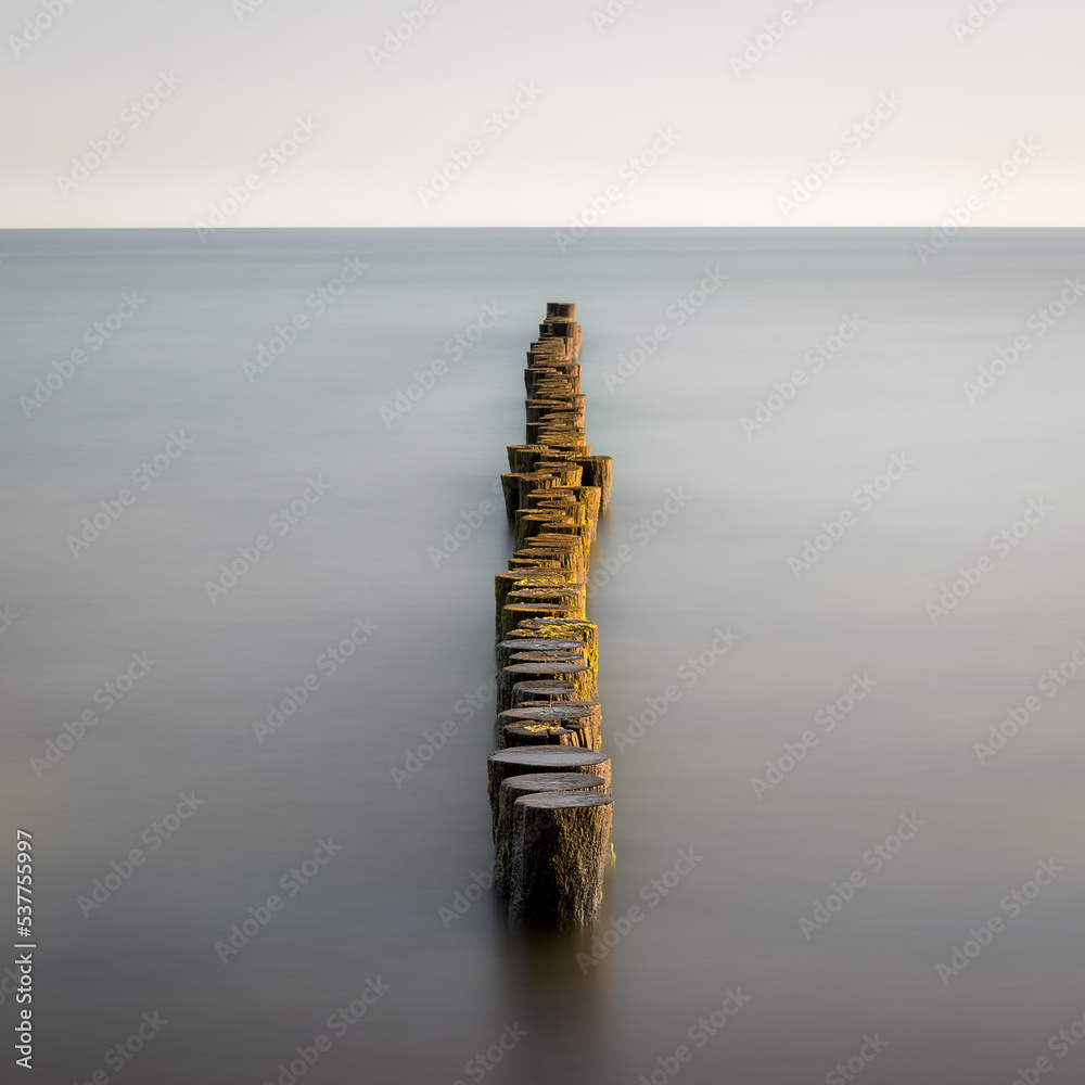 Groynes protruding into the horizon in the Baltic Sea. Long exposure with muted colors. Landscape shot by the sea Groynes protruding into the horizon in the Baltic Sea. Long exposure with muted colors. Landscape shot by the sea