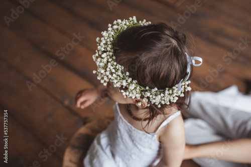 Girl in white summer dress, flower crown and with eco beads sitting in studio
