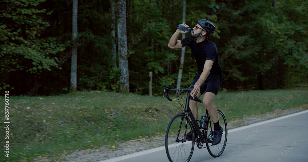 Naklejka premium CU Cyclist drinking water while cycling on an empty forest road