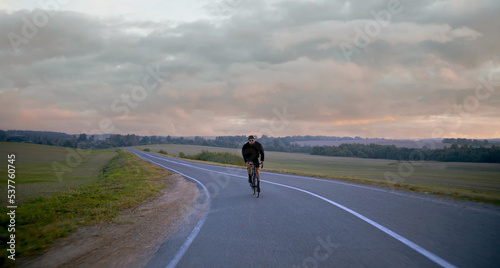 WIDE Cyclist riding his bicycle on an empty rural road at dawn, epic sunrise in the background © supamotion