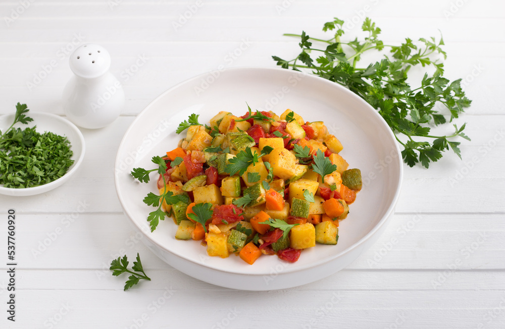 Vegetable stew with zucchini, carrots, potatoes and parsley on a white plate on a light gray background Vegetable stew with zucchini, carrots, potatoes and parsley on a white plate on a light gray background