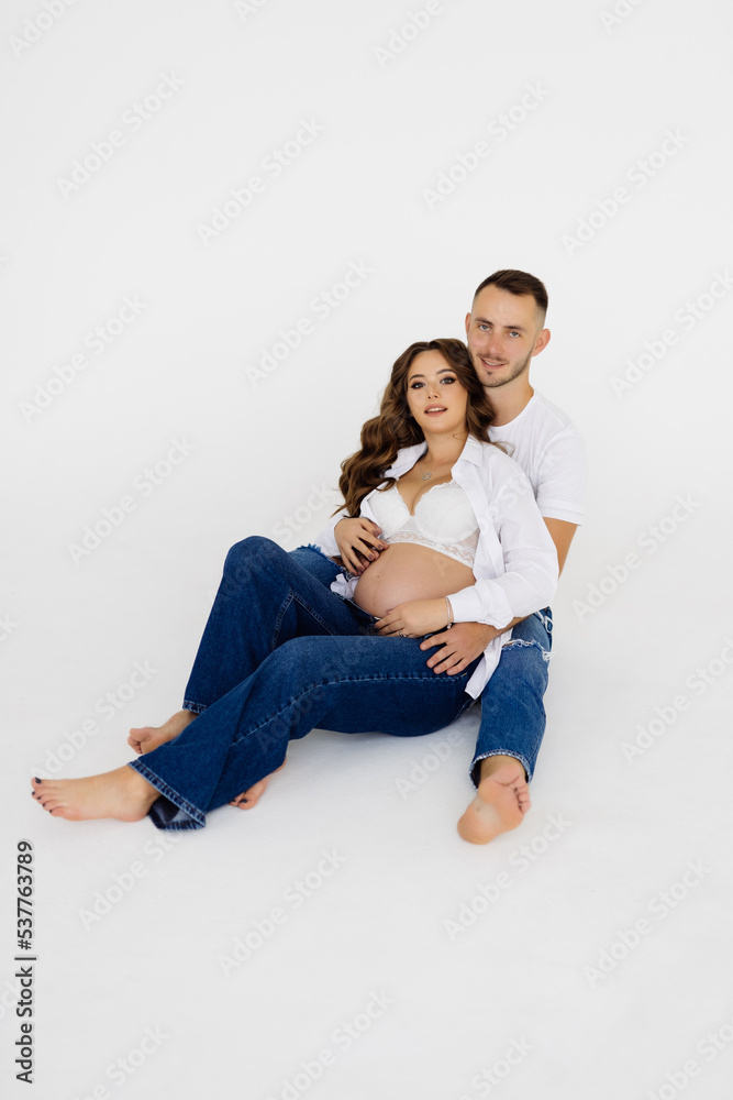 Young Happy pregnant couple sitting on the floor over a white background Young Happy pregnant couple sitting on the floor over a white background