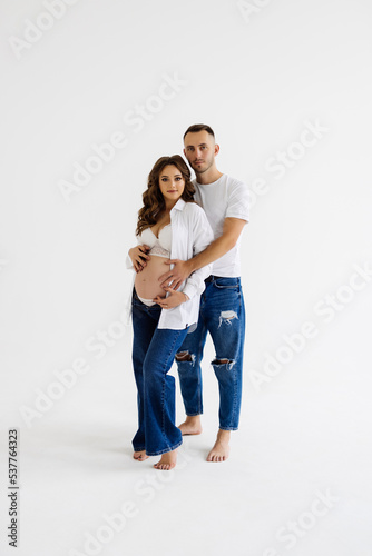 Cheerful young man standing with his pregnant woman isolated over white background wall. Looking aside.