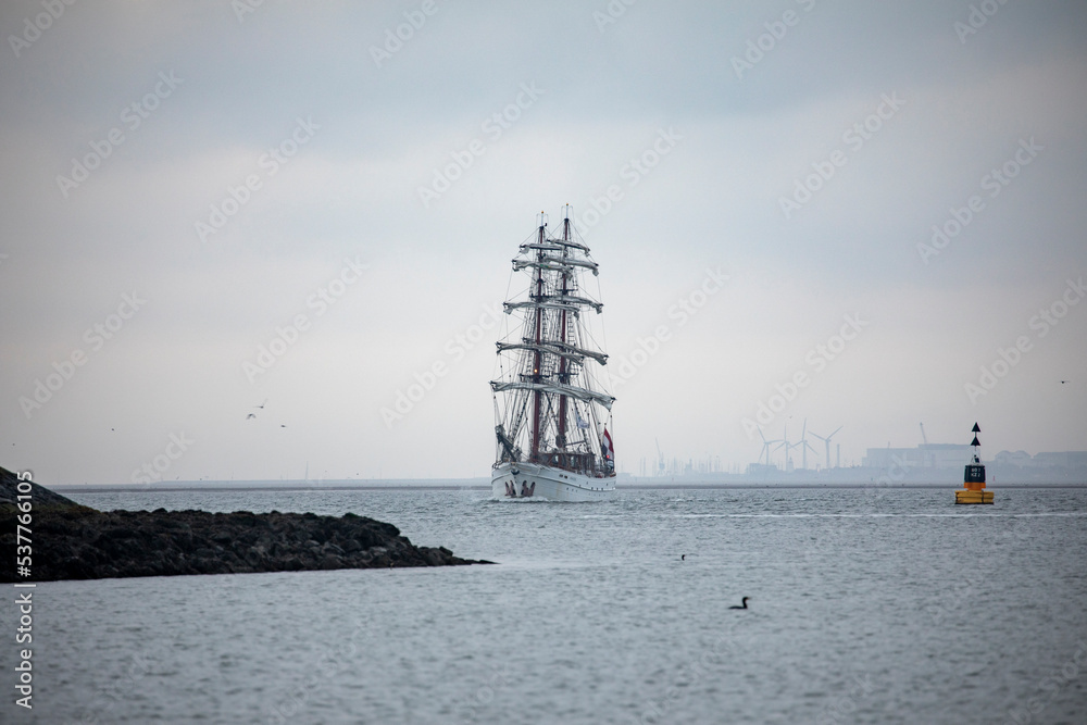 Classic brik approaching harbor out of sea fog with windmills and industry in background Classic brik approaching harbor out of sea fog with windmills and industry in background