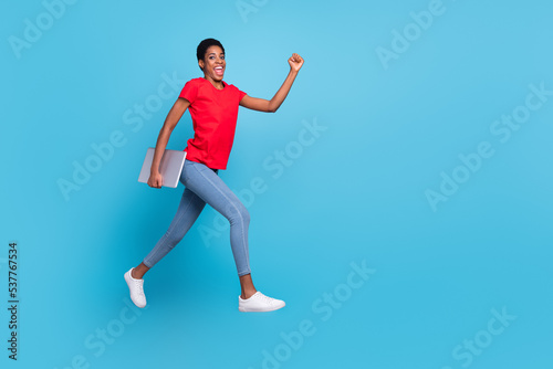 Photo of cute charming short hair person dressed red t-shirt hurrying jumping carrying modern gadget isolated blue color background © deagreez