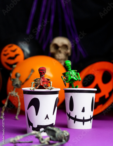 Halloween party. Skeletons coming out from the cup with balloons and skull in the background photo