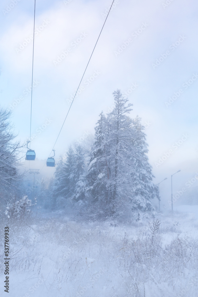 Obraz premium Bansko, Bulgaria winter ski resort with blue gondola lift cabins, forest pine trees and mountains view