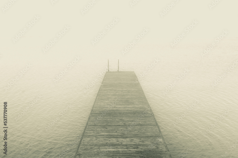 Dreamlike image of wooden jetty on lake in fog
