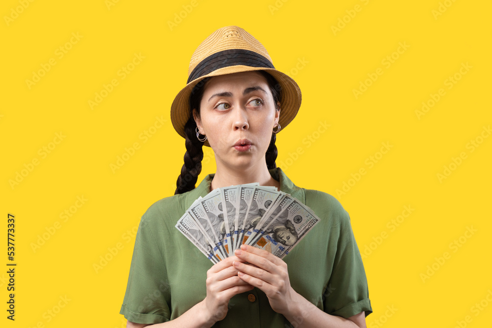 Banking and exchange currency. Portrait of a amazement Caucasian woman wearing straw hat and holding a fan of dollars banknotes. Inflation. The concept of investment and trade market Banking and exchange currency. Portrait of a amazement Caucasian woman wearing straw hat and holding a fan of dollars banknotes. Inflation. The concept of investment and trade market