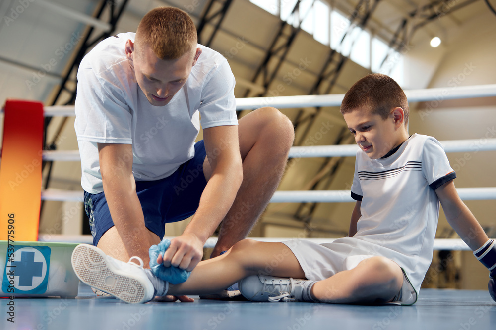Personal coach, team trainer provides first aid to an athlete with a leg injury. Boxing training in the gym. Sport, medicine, studying Personal coach, team trainer provides first aid to an athlete with a leg injury. Boxing training in the gym. Sport, medicine, studying