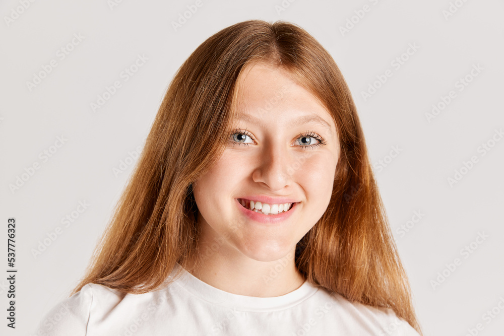 Close-up portrait of young cheerful girl, smiling at camera isolated over grey studio background Close-up portrait of young cheerful girl, smiling at camera isolated over grey studio background