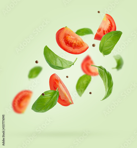 Flying ingredients of tomatoes, basil, black pepper on green background. Italian food