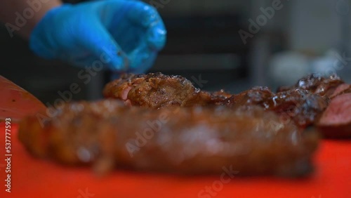 The professional chef cuts perfect juicy beef steak into slices for the course in the restaurant kitchen. Master chef cooks dinner with roasted tender meat pieces and ribs, garnish and greens.