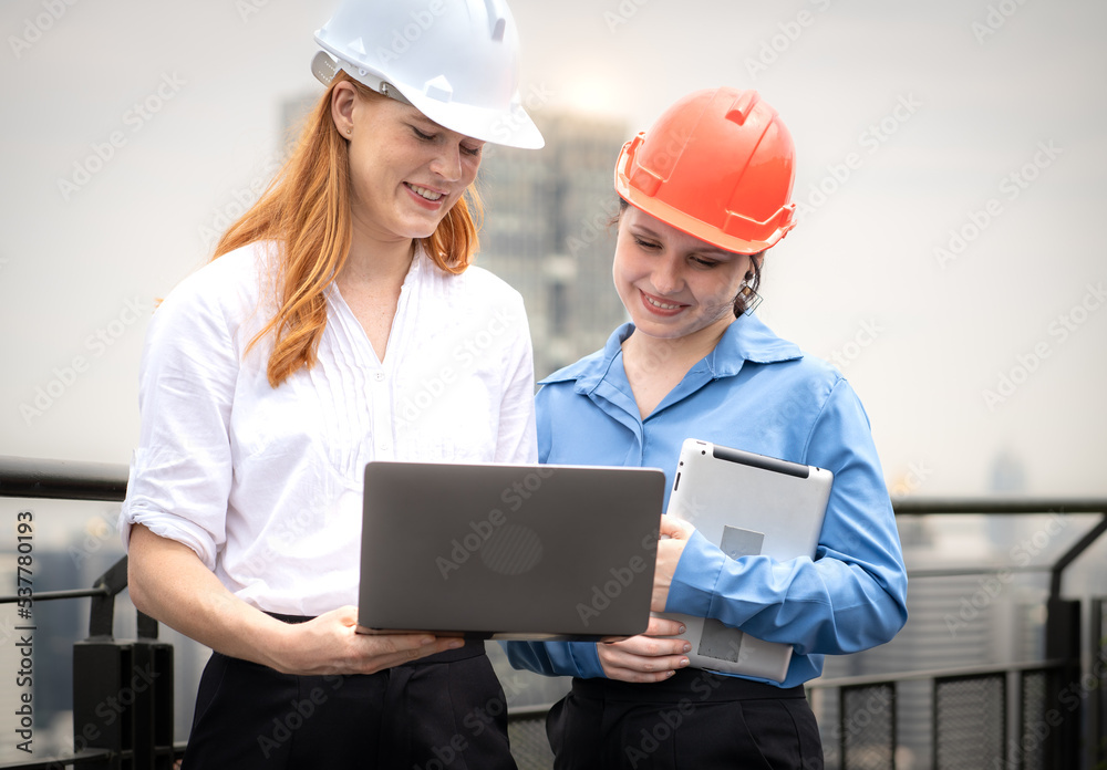Engineer man and architect coworker standing outdoors on rooftop of construction site looking at blueprint for apartment, housing development. Maintenance building contractor discussion with teamwork Engineer man and architect coworker standing outdoors on rooftop of construction site looking at blueprint for apartment, housing development. Maintenance building contractor discussion with teamwork