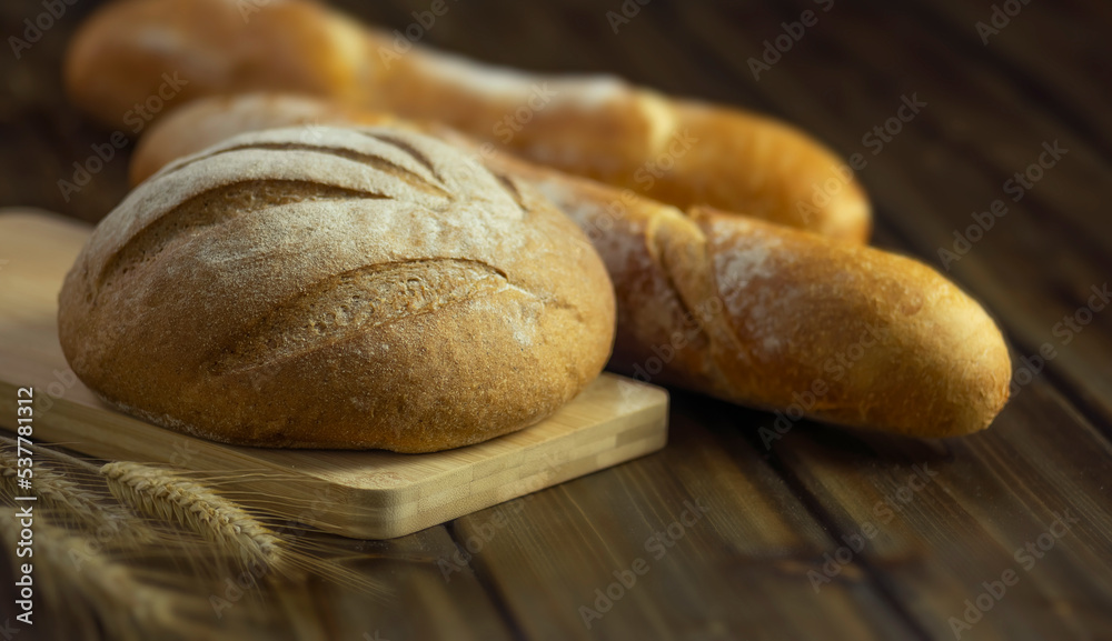 rye round bread on a cutting board and wheat baguette on a table on a wooden background
