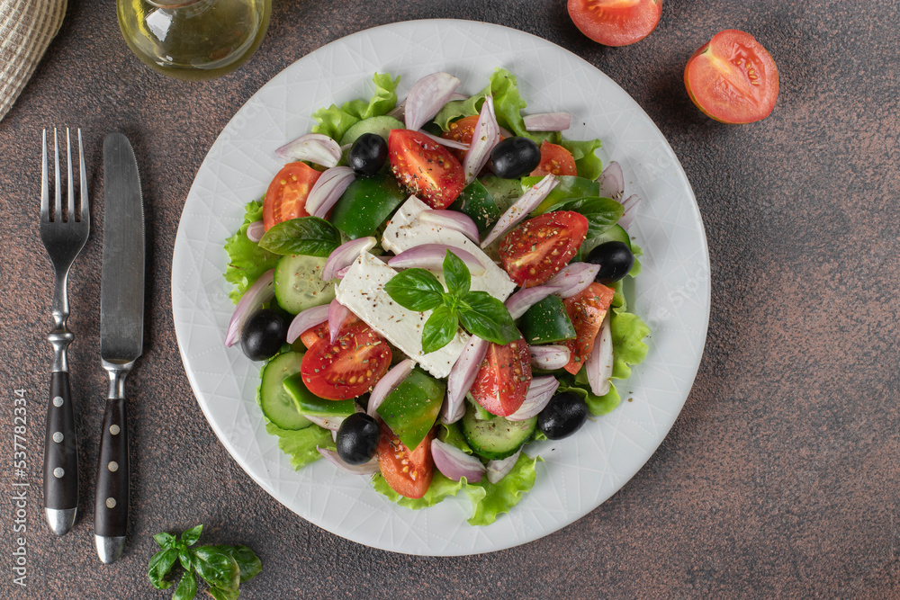 Classic Greek salad from tomatoes, cucumbers, sweet pepper, olives, basil and feta cheese on white plate