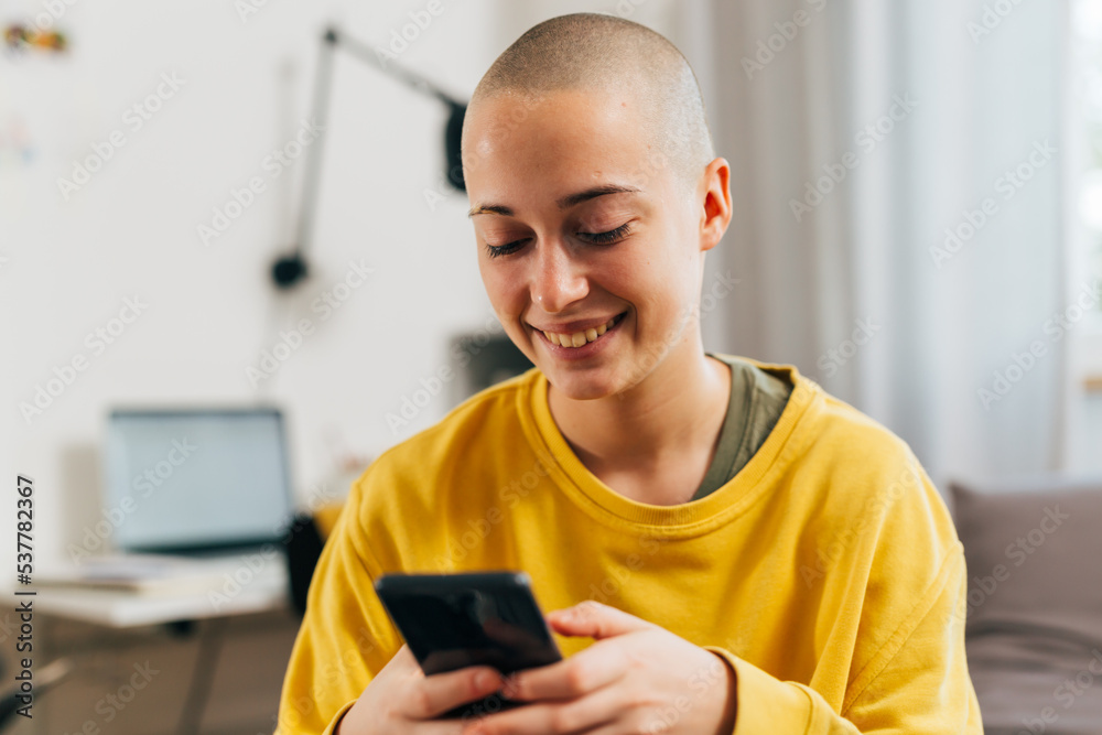 gen z bald female using mobile phone in her room gen z bald female using mobile phone in her room