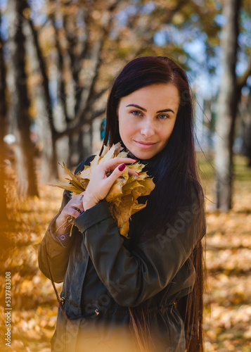 Beautiful Ukrainian girl in the autumn park. Brunette in the park with a bouquet of maple leaves. Autumn  fall. Sunny day in autumn park