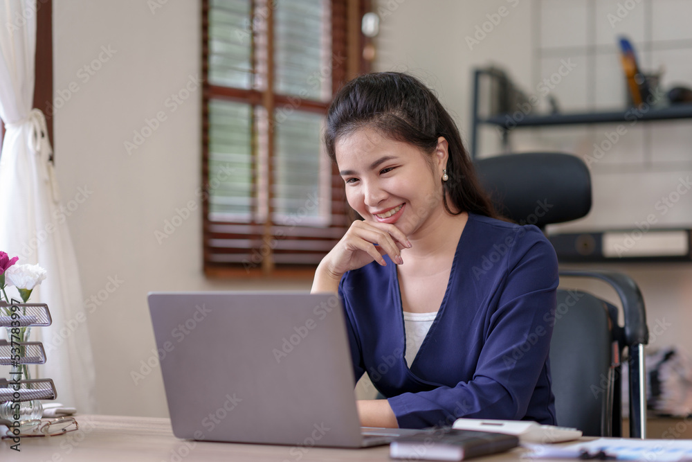 Obraz premium Attractive Asian businesswoman using laptop in office Take notes of work details, smile brightly.
