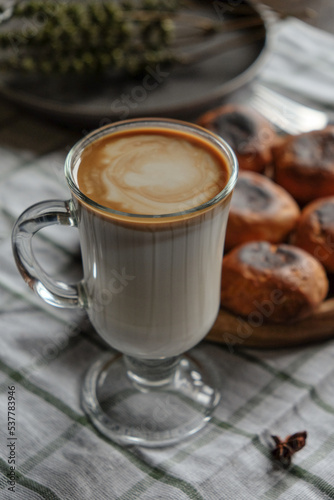 Scones on a wooden plate with fork, coffee and milk in a glass cup. On a white checkered towel