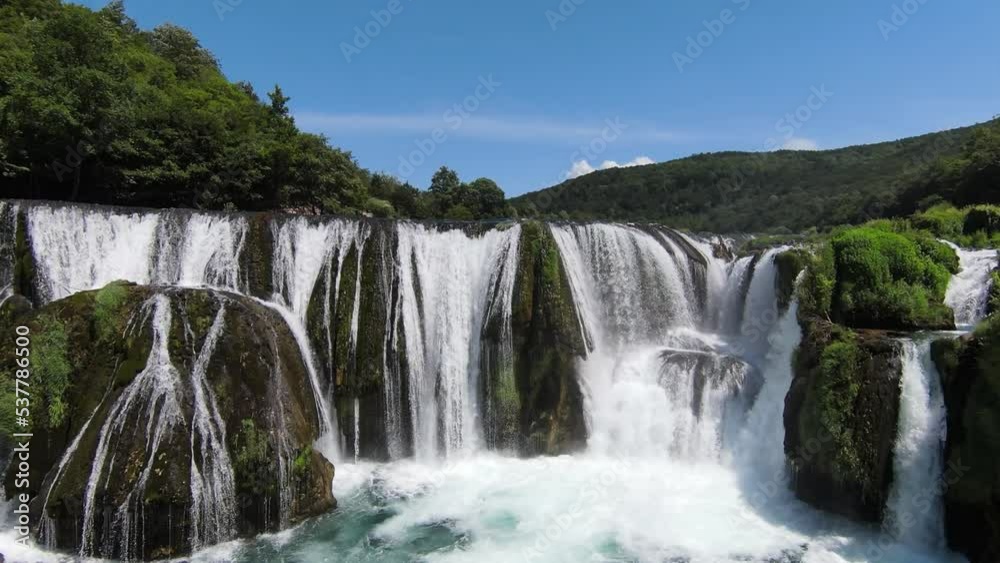 FPV Aerial shot skilled flying at natural landscape river Una with waterfall Strbacki Buk in the dense green forest under trees.