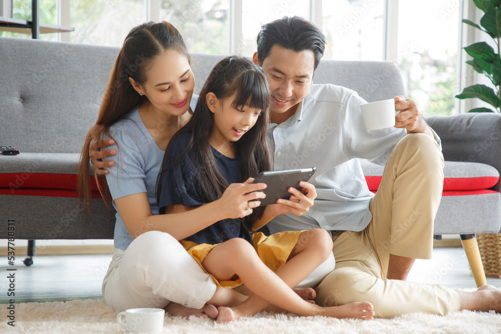 Happy young asian family mom and dad with daughter having fun in liviing room at home, while daughter using tablet. Family,love and happiness concept.