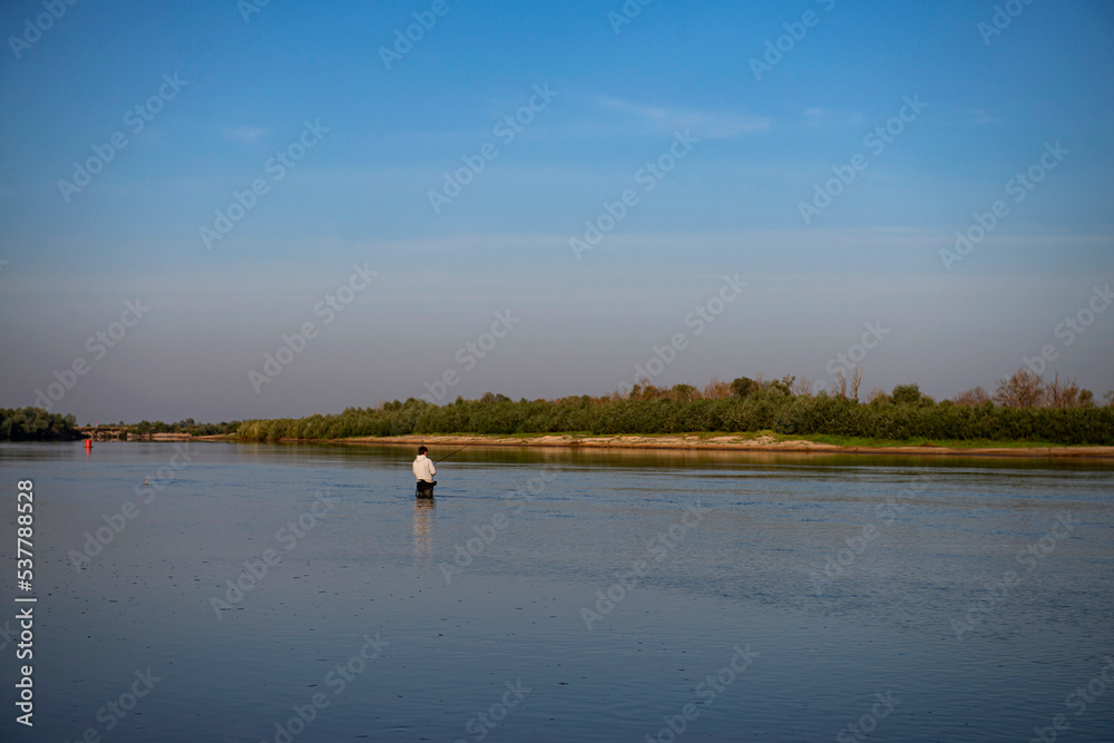 A fly-fishing fisherman on the river in summer.fly fishing fisherman in a gray jacket fishing in the middle of the river in the river in summer.copy space.bright advertising of fishing gear production