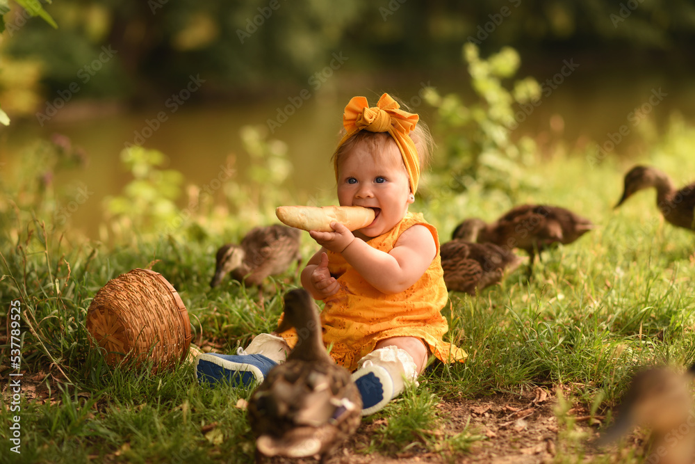 little girl in the park feeds the ducks. The child plays with ducks. Girl in a yellow dress eats bread little girl in the park feeds the ducks. The child plays with ducks. Girl in a yellow dress eats bread