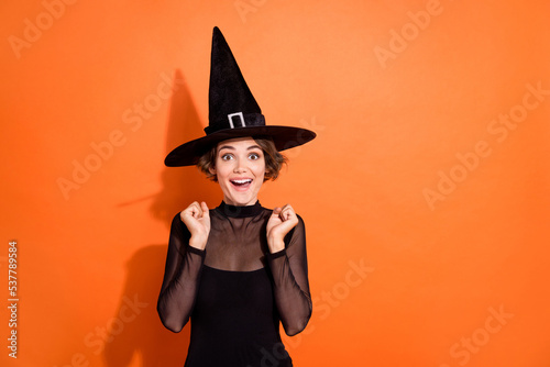 Photo of funky lucky girl dressed black gothic dress headwear rising fists empty space isolated orange color background photo