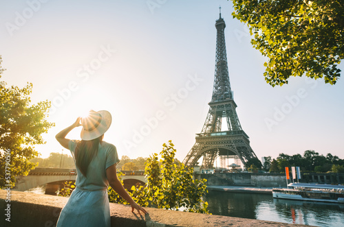 Rear view of woman tourist in sun hat standing in front of Eiffel Tower in Paris at sunset. Travel in France, tourism concept. Holiday or vacation in Paris © Creative Cat Studio