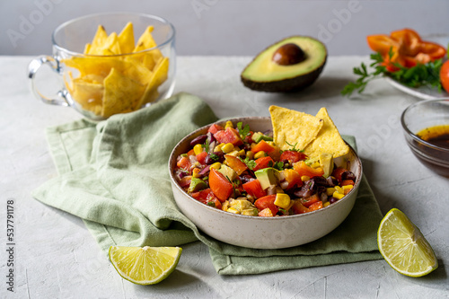 Cowboy caviar is traditional Mexican vegetable salad in bowl with ingredients and nachos on concrete background 