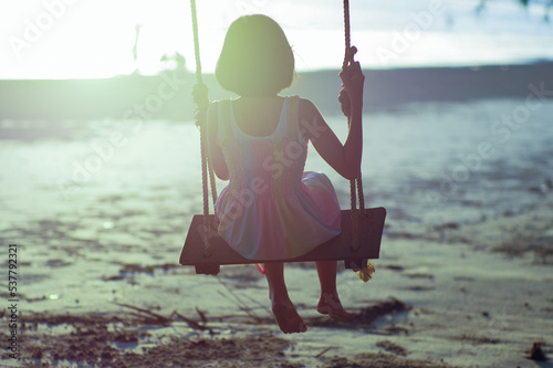 Rear view of lonely Asian girl sits on the wooden swing with sunset in background