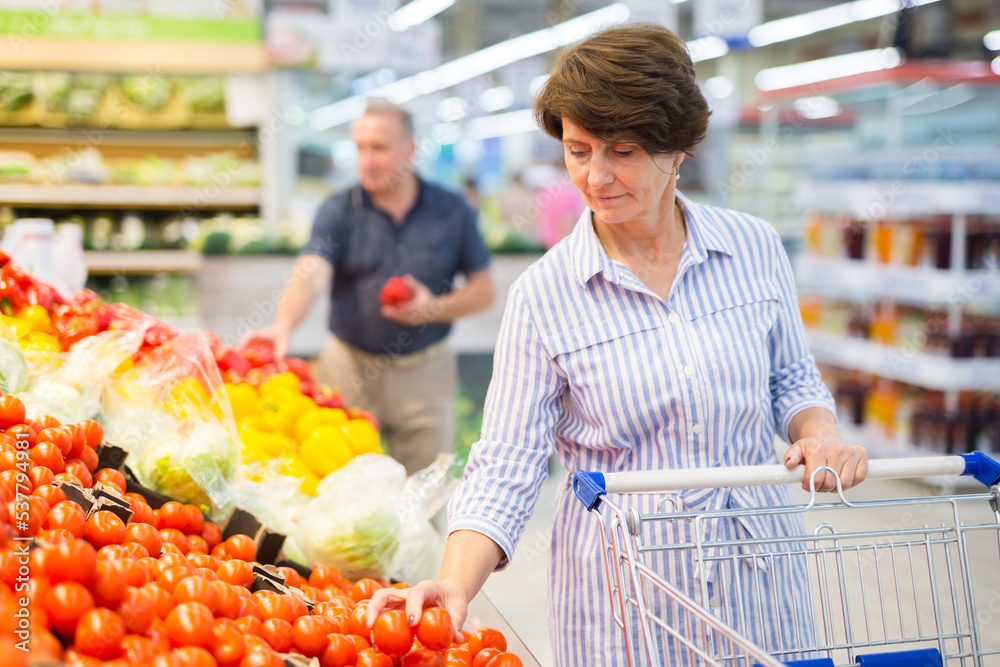 Elderly retired senora buying tomatoes in grocery section of the supermarket