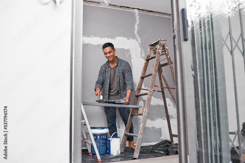 Ultra wide shot of Asian man painting a wall doing home renovation