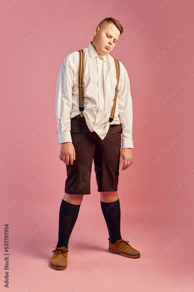 Sleep. Studio shot of cute big obese teen boy in white shirt and shorts with suspenders isolated over pink background. Emotions, retro fashion, dieting Sleep. Studio shot of cute big obese teen boy in white shirt and shorts with suspenders isolated over pink background. Emotions, retro fashion, dieting
