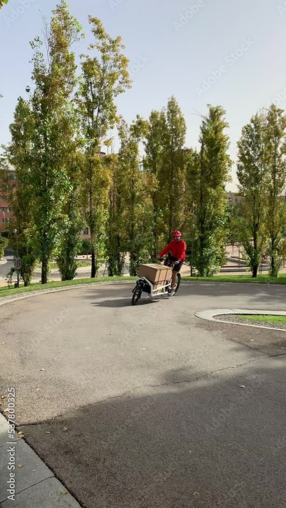 young messenger with red clothes and helmet riding a cargo bike to make a shipment on a bike lane in a city, horizontal video young messenger with red clothes and helmet riding a cargo bike to make a shipment on a bike lane in a city, horizontal video