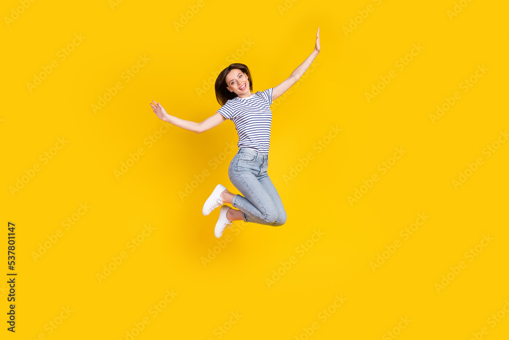Full length photo of nice young girl spread hands plane jumping ad poster wear stylish striped garment isolated on yellow color background