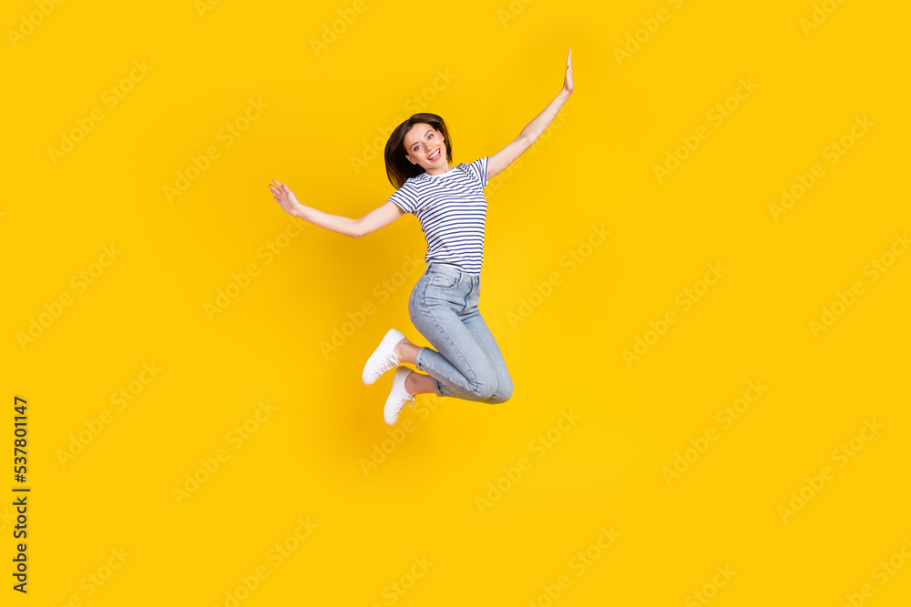 Obraz premium Full length photo of nice young girl spread hands plane jumping ad poster wear stylish striped garment isolated on yellow color background