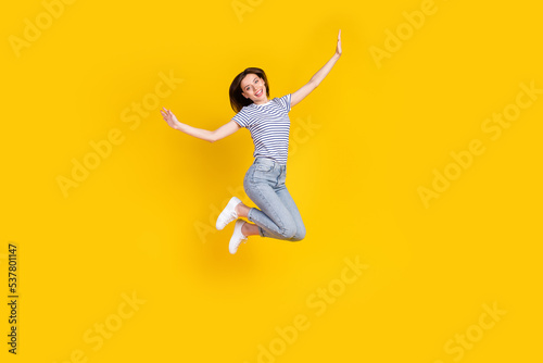Full length photo of nice young girl spread hands plane jumping ad poster wear stylish striped garment isolated on yellow color background © deagreez